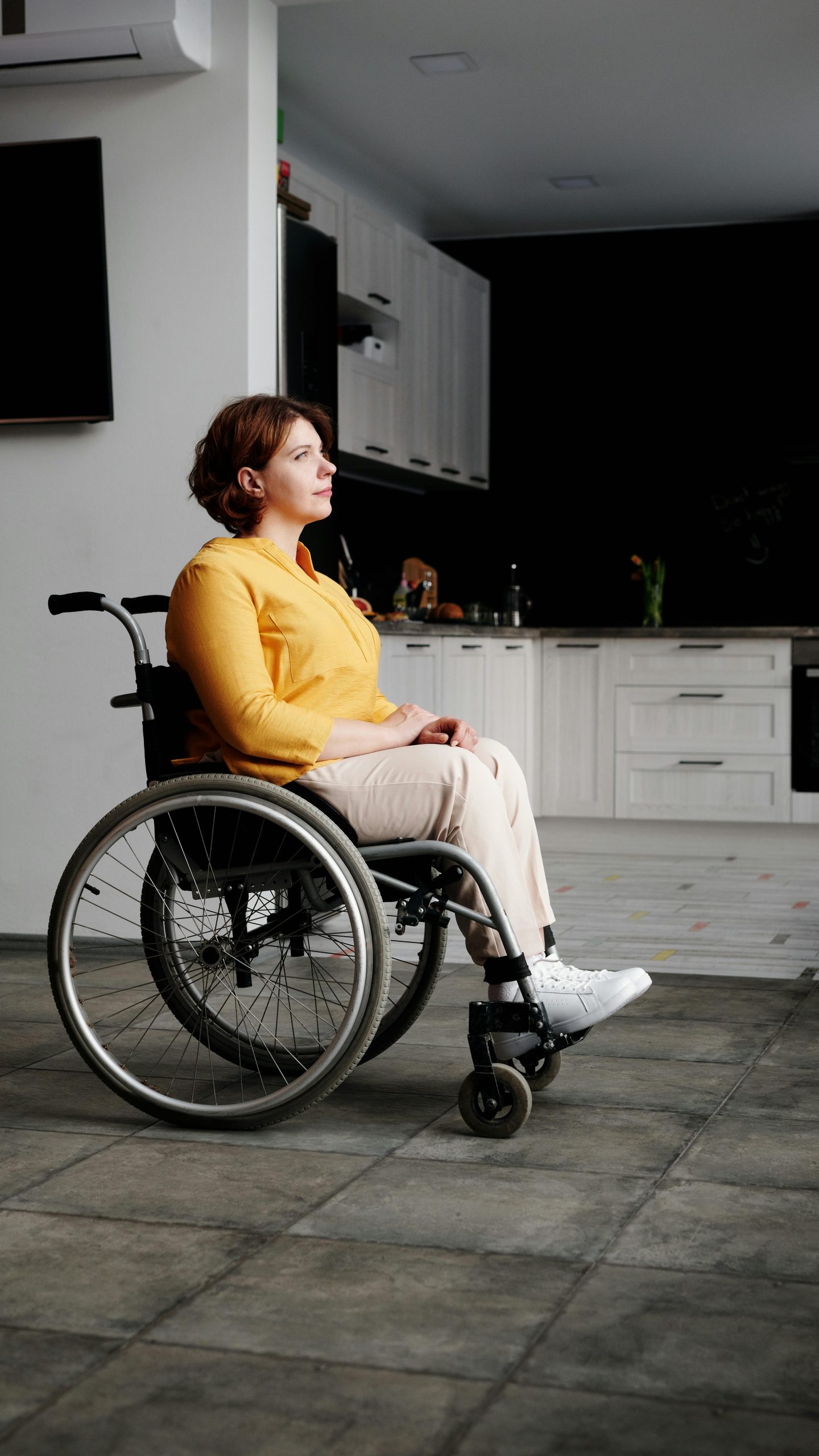 Woman in wheelchair gazing thoughtfully in a modern kitchen setting.