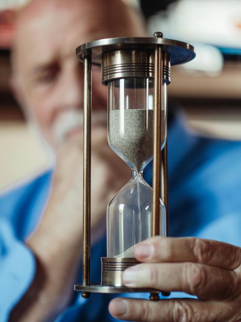 Elderly man holding a metal hourglass, focusing on the sand timer.